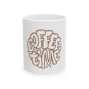 Peut inclure: Tasse à café en céramique blanche avec l'inscription "COFFEE TIME" en marron, dans une police de style bulle. Le texte est disposé en cercle. La tasse est de taille et de forme standard.