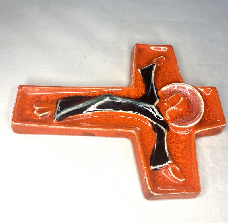 May include: Orange ceramic wall cross with a black and white figure of Jesus Christ. The cross has a textured surface.