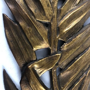 May include: A gold-colored metal wall decor in the shape of a stylized fern leaf.