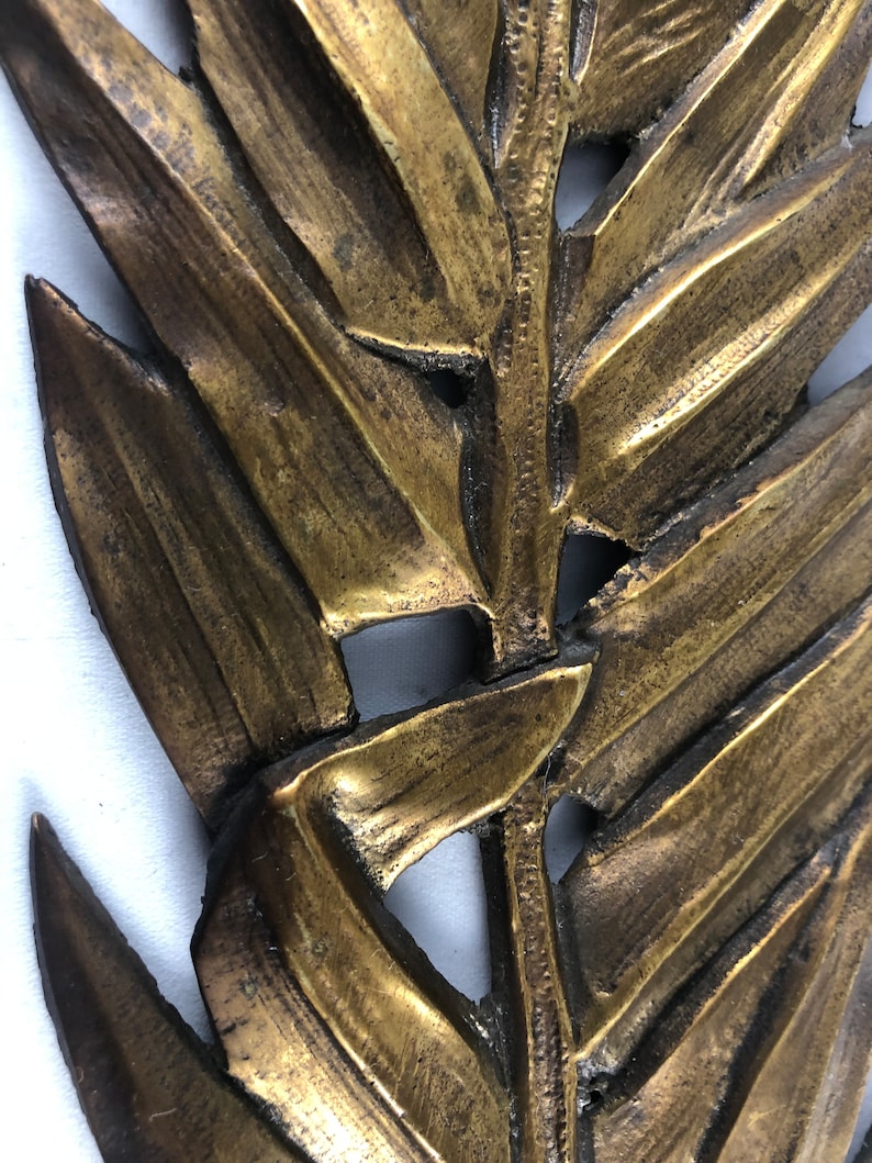 May include: A gold-colored metal wall decor in the shape of a stylized fern leaf.