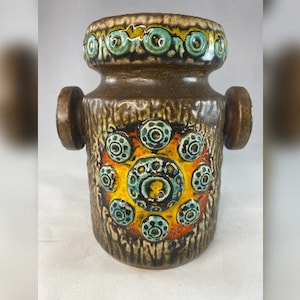 Può includere: Un vaso in ceramica marrone con una superficie strutturata e un motivo geometrico di cerchi blu, gialli e arancioni. Il vaso ha due piccole maniglie sui lati.