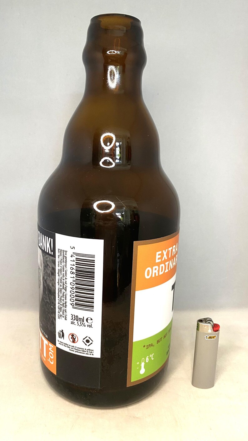 May include: A brown glass beer bottle with a white and black label, and the words "EXTRA ORDINARY" in orange. The bottle contains 330ml of beer and is next to a silver BIC lighter.
