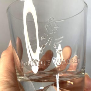 Puede incluir: Un vaso bajo transparente con el logotipo "Johnnie Walker" grabado en el lateral. El vaso presenta un dise&ntilde;o de base geom&eacute;trica y una forma de vaso cl&aacute;sico, adecuado para whisky u otros licores.