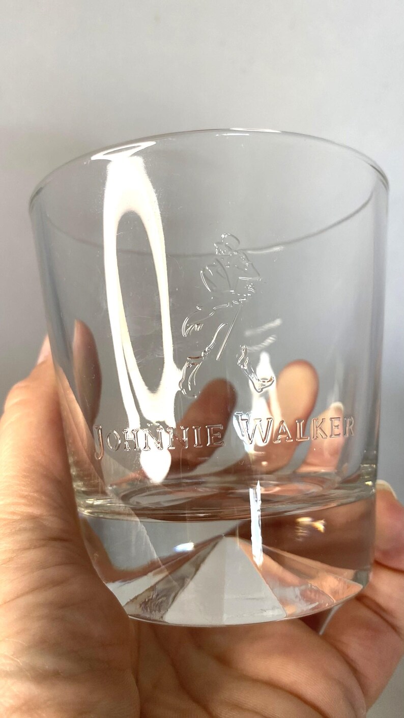 Puede incluir: Un vaso bajo transparente con el logotipo "Johnnie Walker" grabado en el lateral. El vaso presenta un dise&ntilde;o de base geom&eacute;trica y una forma de vaso cl&aacute;sico, adecuado para whisky u otros licores.