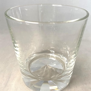 Puede incluir: Vaso de vidrio transparente y vac&iacute;o con base facetada. El vaso tiene una forma ligeramente acampanada y un logotipo grabado cerca de la parte superior. La base del vaso tiene un patr&oacute;n en forma de diamante.