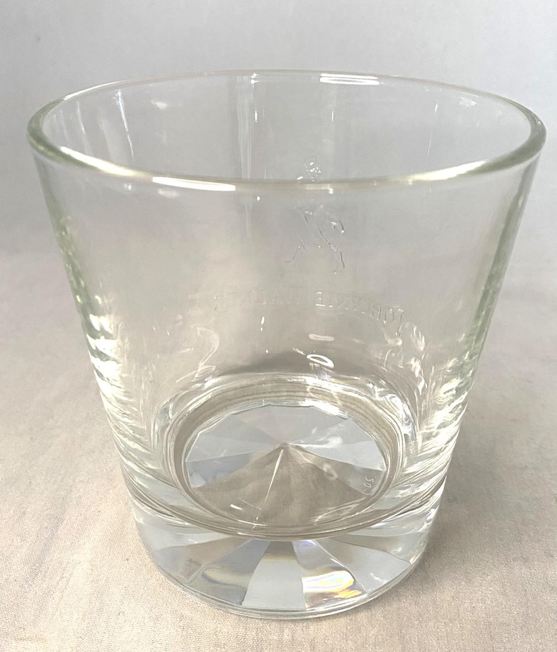 Puede incluir: Vaso de vidrio transparente y vac&iacute;o con base facetada. El vaso tiene una forma ligeramente acampanada y un logotipo grabado cerca de la parte superior. La base del vaso tiene un patr&oacute;n en forma de diamante.