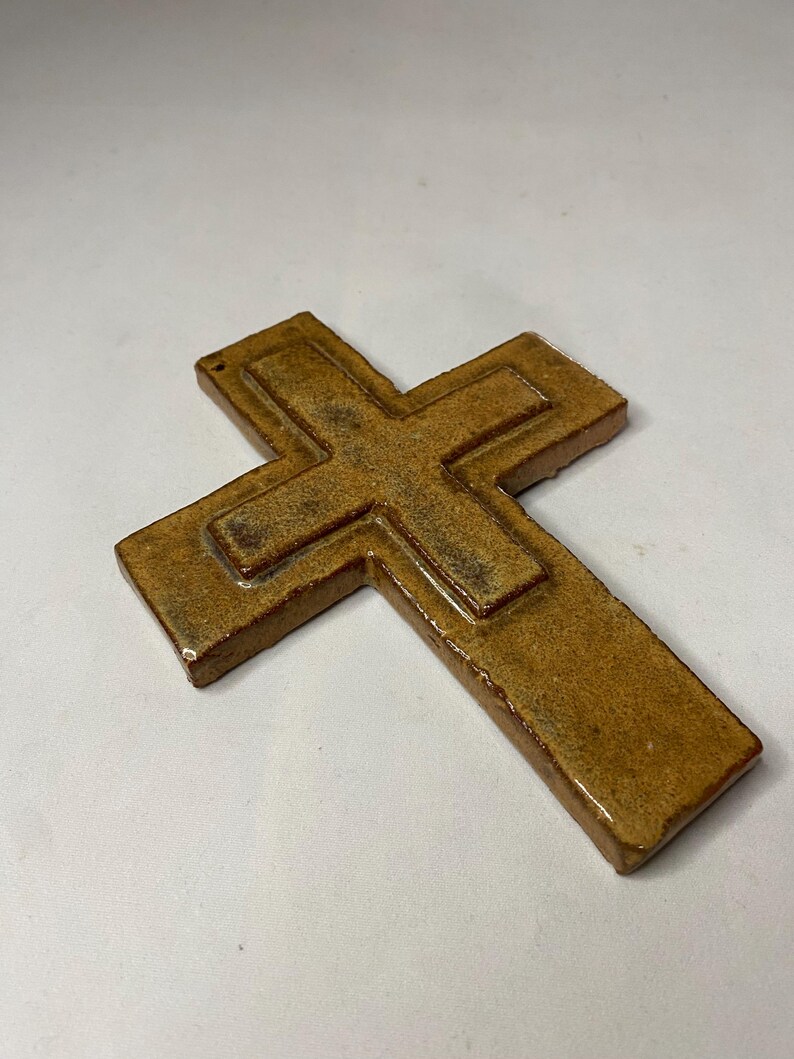 May include: A brown ceramic cross with a raised design. The cross has a rustic, aged look.