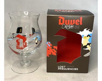 May include: A clear glass beer goblet with a wide bowl and a stem, next to a brown box. The glass has a colorful design with the letter "D" and cartoon figures. The box reads "Duvel Collection Limited Edition" and "Lost Frequencies".