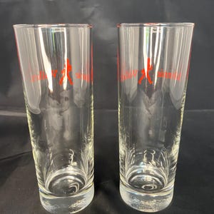 Może przedstawiać: Dwa przezroczyste szklane kieliszki do picia z czerwoną sylwetką osoby grającej w baseball i tekstem "Miller High Life" nadrukowanym na przodzie każdego kieliszka.