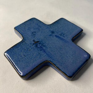 K&ouml;nnte beinhalten: Ein blaues Keramikkreuz mit leicht strukturierter Oberfl&auml;che. Das Kreuz hat eine dunkelblaue Glasur mit einem Hauch von Lila.