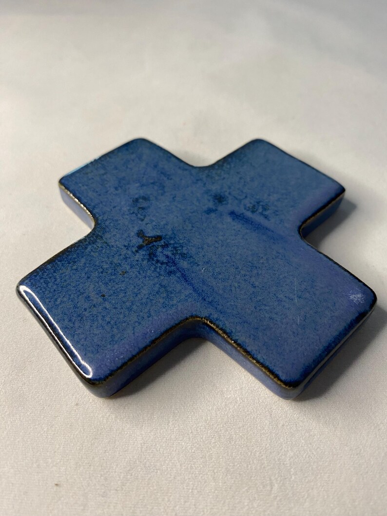 K&ouml;nnte beinhalten: Ein blaues Keramikkreuz mit leicht strukturierter Oberfl&auml;che. Das Kreuz hat eine dunkelblaue Glasur mit einem Hauch von Lila.