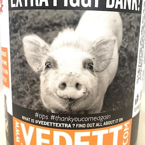 May include: A brown bottle with a black and orange label featuring a black and white image of a pig's face. The label reads "EXTRA PIGGY BANK!" and includes the text "#tips #thankyoucomeagain".