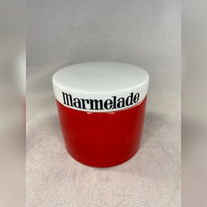 May include: A red ceramic jar with a white lid and the word "Marmalade" printed on the lid.