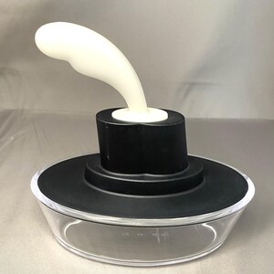 May include: A clear glass container with a black lid and a white, curved handle. The handle is attached to a black cylinder on top of the lid. The container has measurement markings on the side.