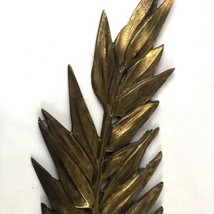 May include: A gold-colored metal leaf design with a detailed, textured surface. The leaf is a decorative element that could be used for a variety of purposes, such as a wall hanging or a craft project.