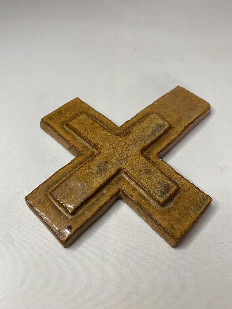 May include: A brown ceramic cross with a raised design. The cross is made of a textured clay and has a rustic look.