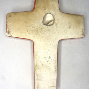 May include: A ceramic cross with a red border and a white center. The cross has a hole in the center for hanging.