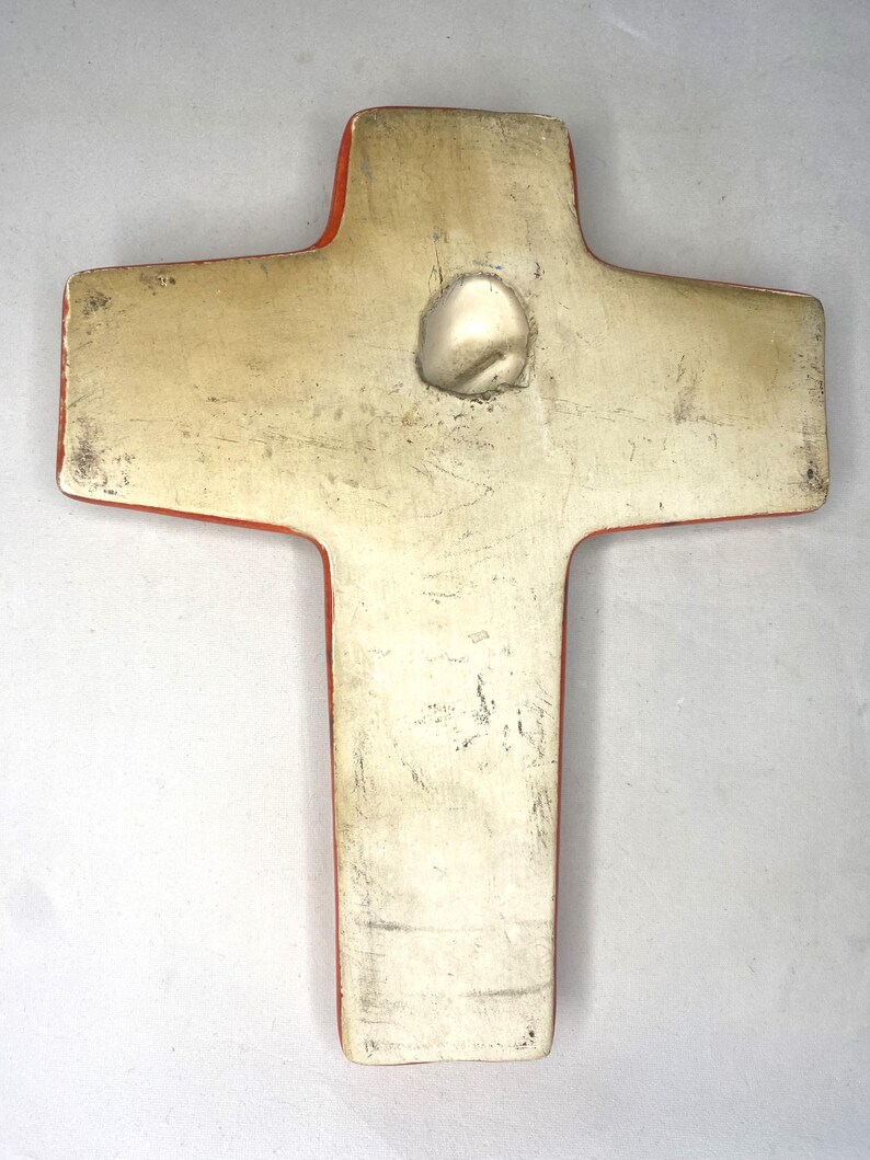 May include: A ceramic cross with a red border and a white center. The cross has a hole in the center for hanging.