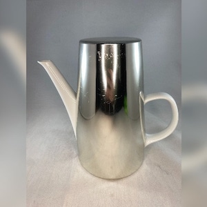 May include: A silver and white ceramic coffee pot with a spout and a handle. The pot has a shiny, metallic finish.