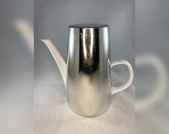 May include: A silver and white ceramic coffee pot with a spout and a handle. The pot has a shiny, metallic finish.