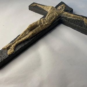 May include: A black ceramic cross with a beige sculpture of a person on it.