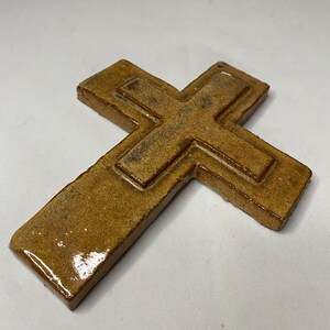 May include: A brown ceramic cross with a raised design. The cross has a glossy finish.