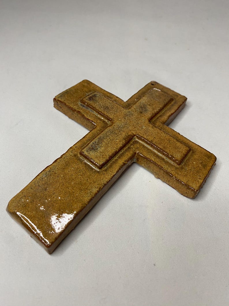 May include: A brown ceramic cross with a raised design. The cross has a glossy finish.