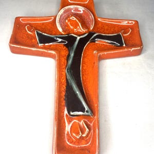 May include: Orange ceramic wall cross with a black and white figure of Jesus Christ on it.