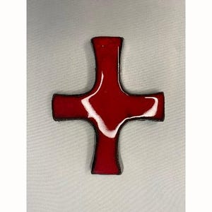 Może przedstawiać: Czerwony ceramiczny krzyż z czarnym obramowaniem. Krzyż jest prosty w designie i ma płaską powierzchnię.