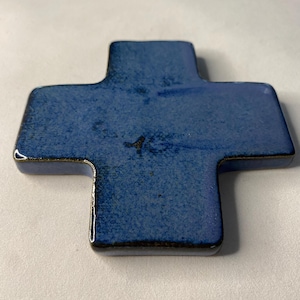 K&ouml;nnte beinhalten: Ein blaues Keramikkreuz mit dunkelblauer Glasur. Das Kreuz ist leicht strukturiert und hat einen dunkelbraunen Rand.