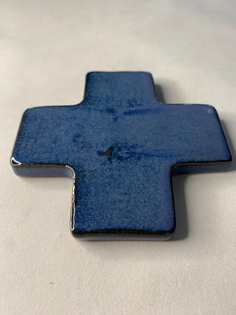 K&ouml;nnte beinhalten: Ein blaues Keramikkreuz mit dunkelblauer Glasur. Das Kreuz ist leicht strukturiert und hat einen dunkelbraunen Rand.