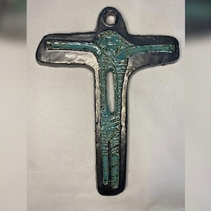 Może przedstawiać: Czarny ceramiczny krzyż z turkusową figurą osoby.