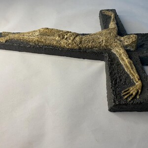 May include: A black and gold ceramic wall sculpture of a person on a cross. The sculpture is textured and has a rough finish.