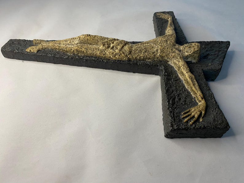 May include: A black and gold ceramic wall sculpture of a person on a cross. The sculpture is textured and has a rough finish.