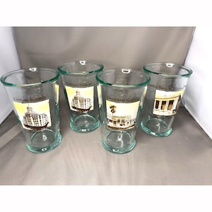 May include: Four clear glass tumblers with green rims. Each glass features a different architectural image with text in Spanish. The text includes "Edificio Bacardi La Habana 1930", "Destileria Bacardi Santiago de Cuba 1930", and "Emilio Bacardi Moreau Santiago de Cuba".