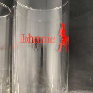 Może przedstawiać: Dwa przezroczyste szklanki z nadrukowanym na boku czerwonym logo Johnnie Walker. Logo przedstawia mężczyznę w pozie chodzenia.