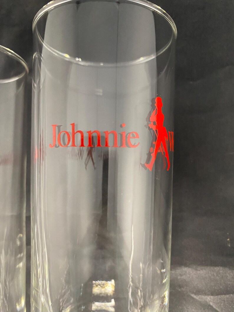 Może przedstawiać: Dwa przezroczyste szklanki z nadrukowanym na boku czerwonym logo Johnnie Walker. Logo przedstawia mężczyznę w pozie chodzenia.