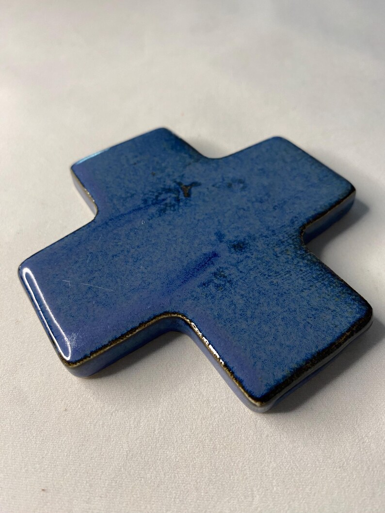 K&ouml;nnte beinhalten: Ein blaues Keramikkreuz mit dunkelbrauner Glasur. Das Kreuz ist leicht erh&ouml;ht und hat eine abgerundete Form.