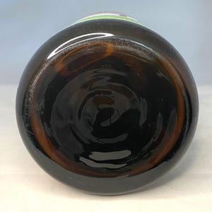 May include: A brown glass bottle, viewed from the bottom, showcasing a dark, swirling interior. The bottle's base has a circular design, and the glass has a slight amber hue. The top of the bottle has a green and white label.