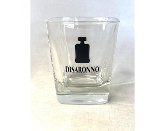 May include: A clear glass rocks glass with the word "DISARONNO" printed on the front. The glass is empty and has a square shape.
