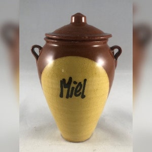 以下が含まれることがあります： 蓋と前面に「Miel」と黒文字で書かれた黄色い円がある茶色の陶器の壺