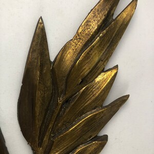 May include: A gold-toned metal leaf design with a textured surface. The leaf is a decorative element that could be used for a variety of purposes, such as a wall hanging or a table centerpiece.