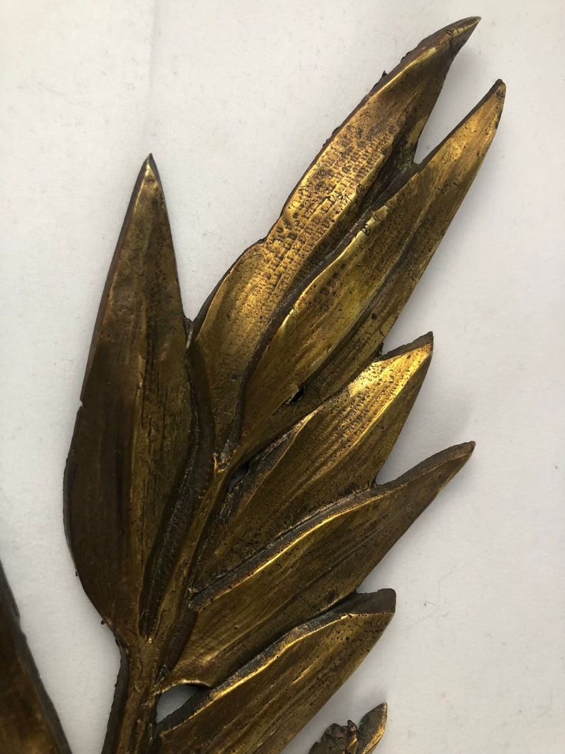 May include: A gold-toned metal leaf design with a textured surface. The leaf is a decorative element that could be used for a variety of purposes, such as a wall hanging or a table centerpiece.