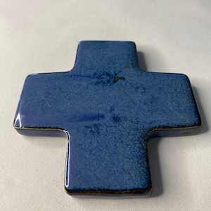 K&ouml;nnte beinhalten: Ein blaues Keramikkreuz mit leicht strukturierter Oberfl&auml;che. Das Kreuz hat einen dunkelblauen Rand.