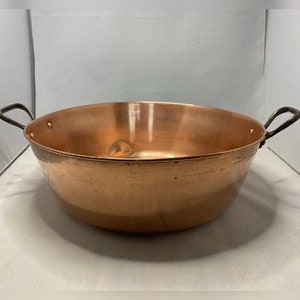 May include: A large copper pot with two handles. The pot has a hammered finish and is slightly dented.