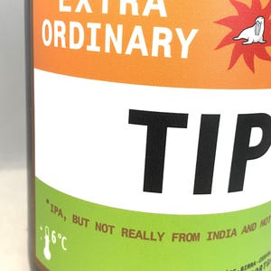 May include: A brown beer bottle with a label that reads "EXTRA ORDINARY TIP". The label has orange, white, and green sections with text and a cartoon seal. The text "IPA, BUT NOT REALLY FROM INDIA AND NOT" is also visible.