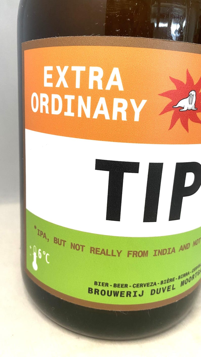 May include: A brown beer bottle with a label that reads "EXTRA ORDINARY TIP". The label has orange, white, and green sections with text and a cartoon seal. The text "IPA, BUT NOT REALLY FROM INDIA AND NOT" is also visible.