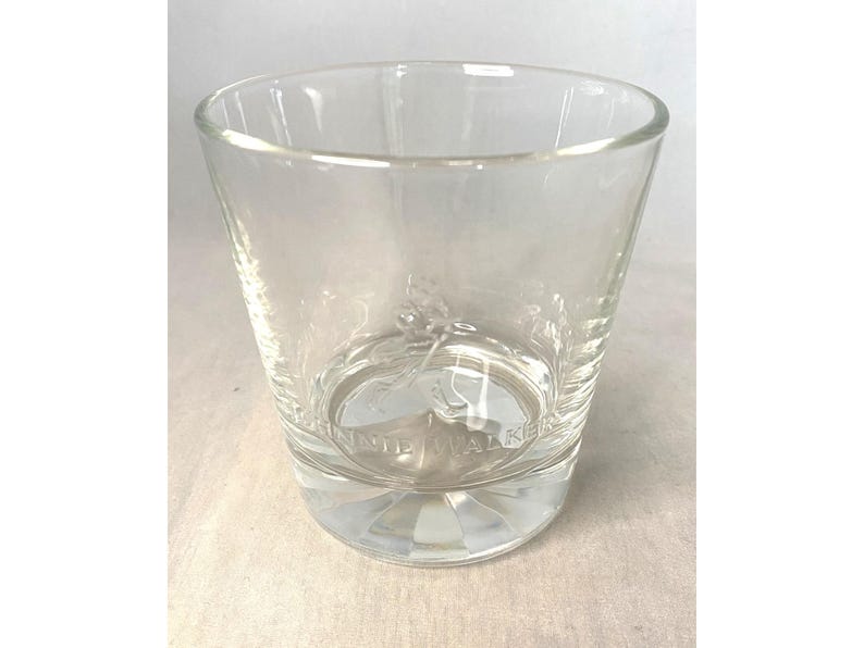 Puede incluir: Un vaso de vidrio transparente y vac&iacute;o con boca ancha y base gruesa estampada. El vaso tiene una forma ligeramente acampanada y un logotipo visible en la parte inferior. El vaso est&aacute; dise&ntilde;ado para beber.