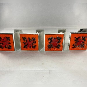 Könnte beinhalten: Vier silberfarbene Gardinenhalter mit orangefarbenen und schwarzen geometrischen Mustern. Die Halter sind quadratisch und haben ein schlichtes, modernes Design.