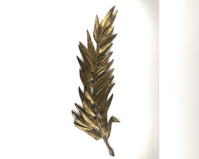 May include: A gold-colored metal leaf wall decor with a detailed design. The leaf is long and narrow with a pointed tip.